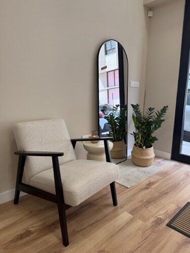 Rincón de espera con sillón de lino, espejo arqueado y plantas